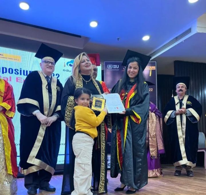 Jyoti in academic robes on stage at a recognition ceremony