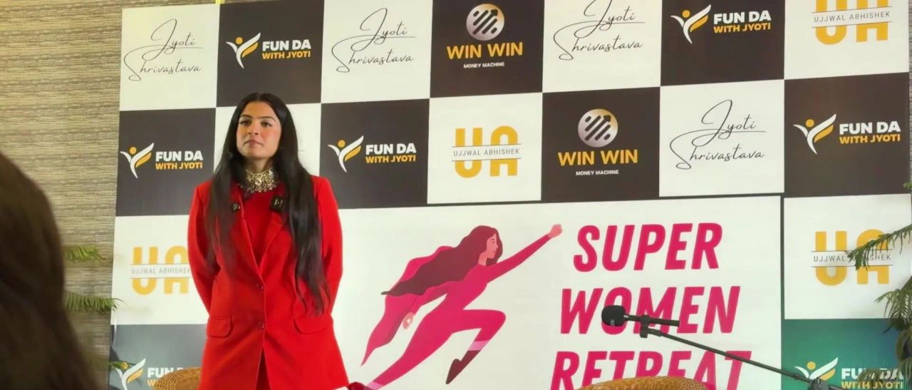 Dr. Jyoti in a red suit on stage in front of the Super Women Retreat backdrop