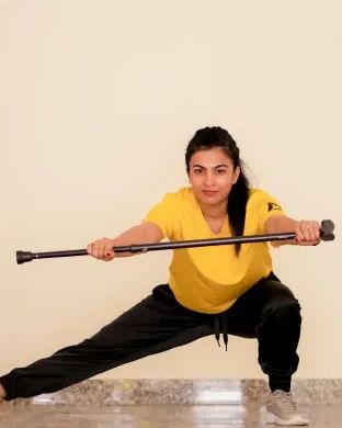 Dr. Jyoti in a lunge, holding a stick overhead during a FunDa stick workout