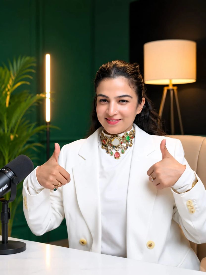 Dr. Jyoti Srivastava in a white blazer, smiling and giving two thumbs up in her studio